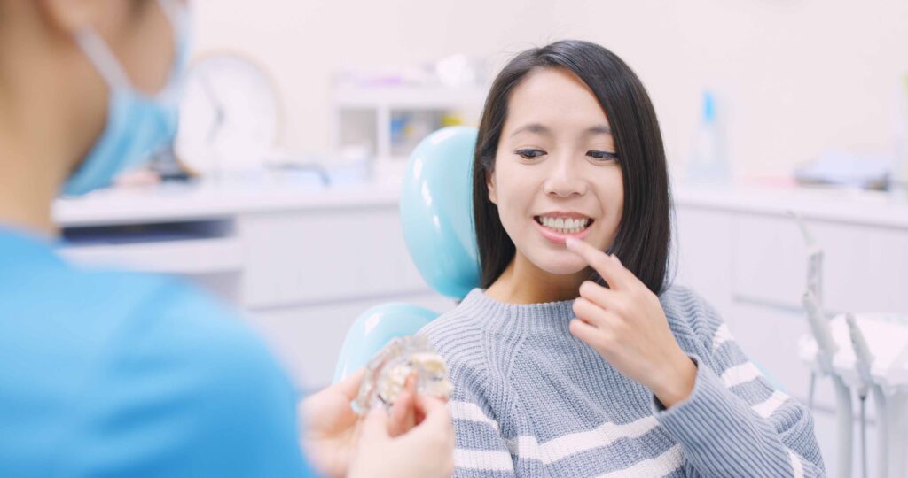 歯科の椅子に座って人差し指で前歯を指差す女性