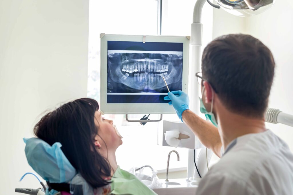 歯のレントゲン写真を見ながら説明する男性歯科医師と歯科の椅子に座って説明を受ける女性