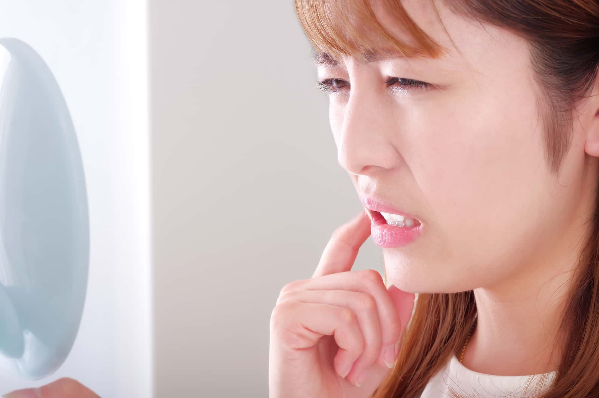 歯がぐらついて鏡を見る女性