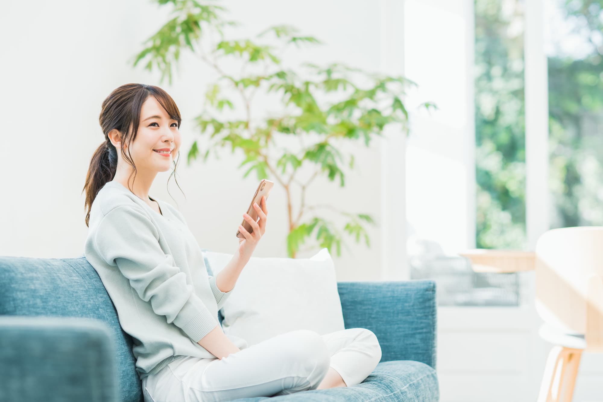 スマホを片手にソファーで寛ぐ女性